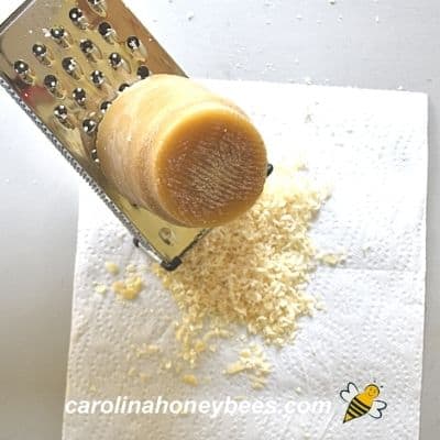 Using kitchen grater to grate raw beeswax block
