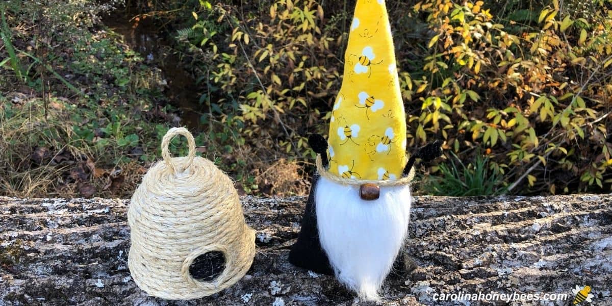 Handmade bee skep and honey bee gnome craft sitting on log image.