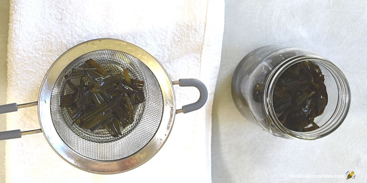 Using metal strainer to remove plantain leaves from infused oil.