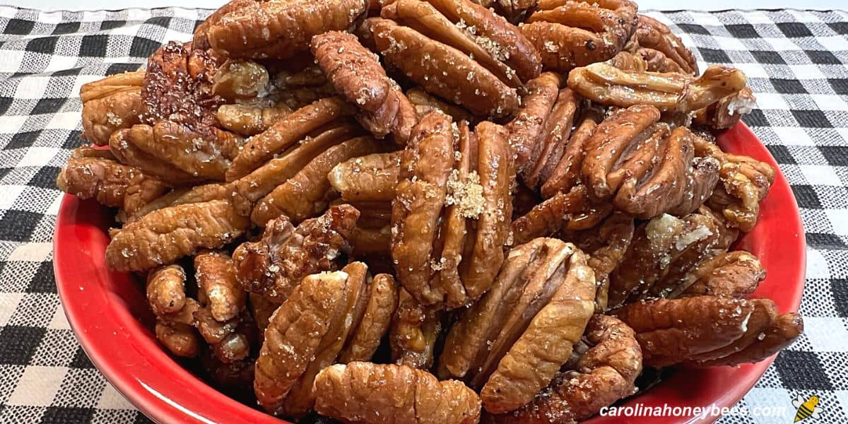 Red dish of honey roasted pecans with brown sugar sprinkle.