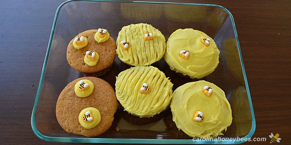 Six homemade cupcakes with bee decorations in a glass storage bowl,