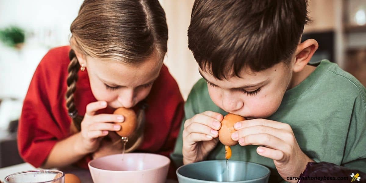 Two kids blowing out liquid inside of eggs before making candles.