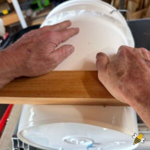 Using piece of wood and pressure to flatten area of honey bucket.